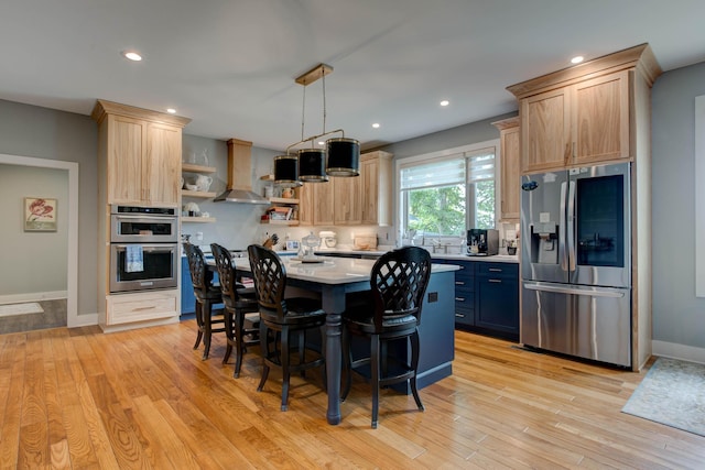 kitchen featuring stainless steel appliances, wall chimney exhaust hood, and light brown cabinetry