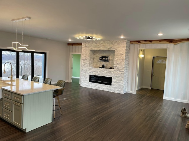 kitchen featuring dark hardwood / wood-style floors, pendant lighting, a fireplace, an island with sink, and a kitchen breakfast bar