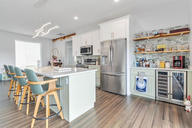 kitchen with a breakfast bar, white cabinetry, hanging light fixtures, a kitchen island with sink, and stainless steel appliances