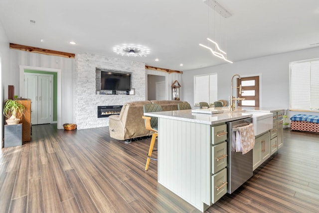 kitchen with a stone fireplace, dishwasher, an island with sink, dark hardwood / wood-style flooring, and decorative light fixtures