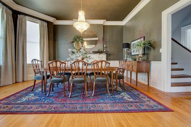 dining space with wainscoting, hardwood / wood-style flooring, an inviting chandelier, stairs, and crown molding