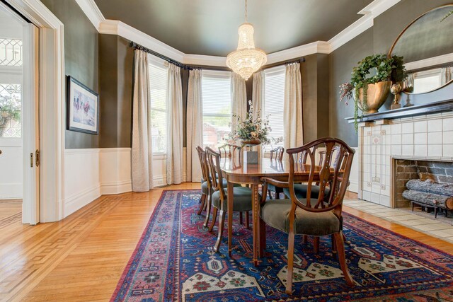 dining space with an inviting chandelier, a tiled fireplace, ornamental molding, and light hardwood / wood-style floors