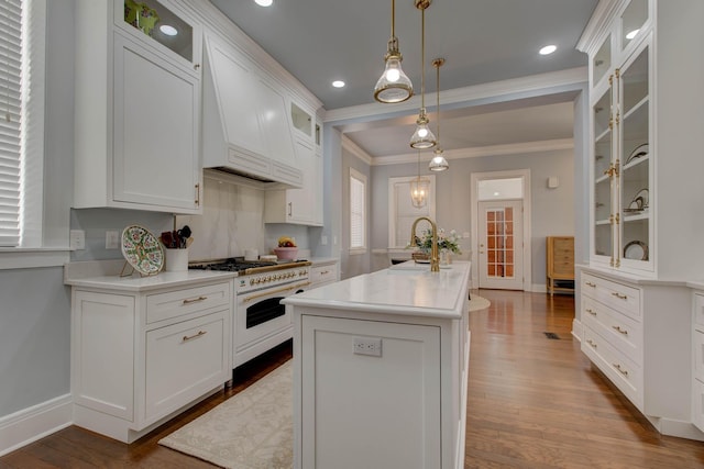 kitchen featuring glass insert cabinets, light countertops, a kitchen island with sink, and white range