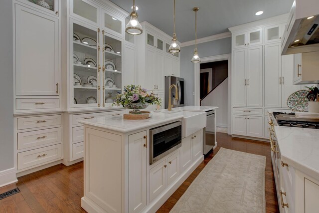 kitchen with decorative light fixtures, light stone countertops, an island with sink, dark wood-type flooring, and wall chimney exhaust hood