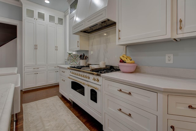 kitchen with dark wood finished floors, glass insert cabinets, light stone counters, double oven range, and white cabinetry