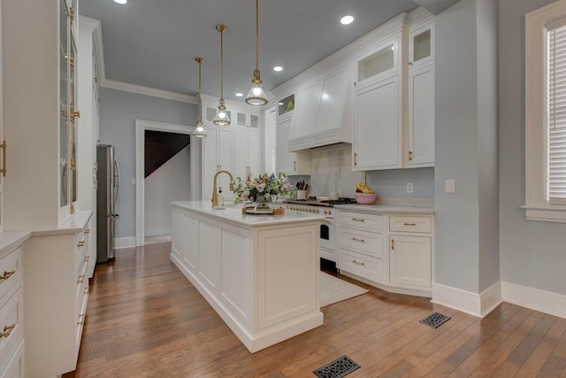 kitchen with light countertops, glass insert cabinets, freestanding refrigerator, a kitchen island with sink, and high end white range oven