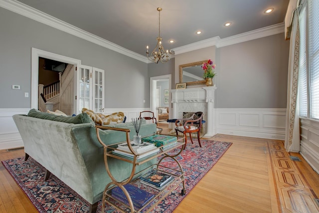 living area featuring light wood finished floors, wainscoting, stairway, a fireplace, and a chandelier