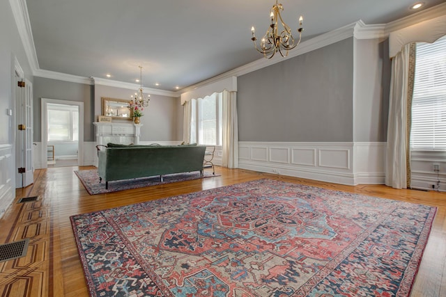 living area with visible vents, ornamental molding, a notable chandelier, and wainscoting