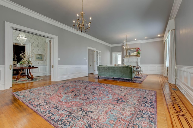 living area featuring a wainscoted wall, light wood finished floors, a decorative wall, ornamental molding, and a chandelier