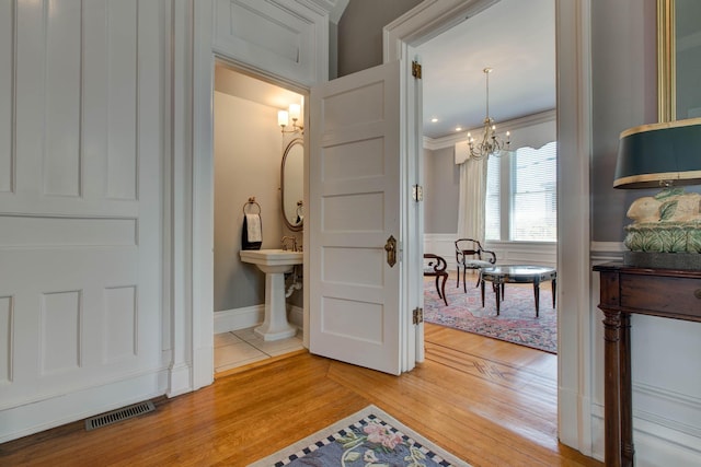 hallway featuring a chandelier, a decorative wall, wood finished floors, visible vents, and ornamental molding