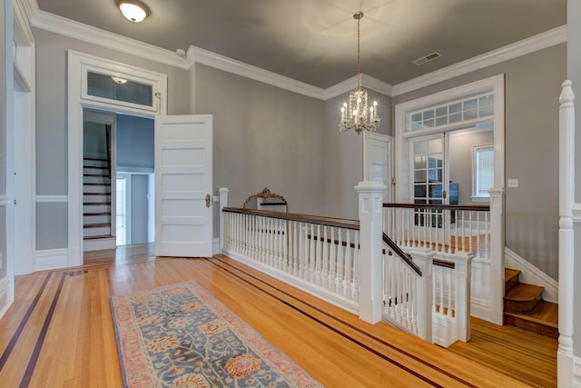 hallway with stairs, visible vents, wood finished floors, and ornamental molding