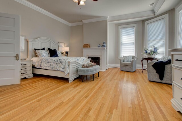 bedroom featuring ceiling fan, a fireplace, light wood-type flooring, and crown molding