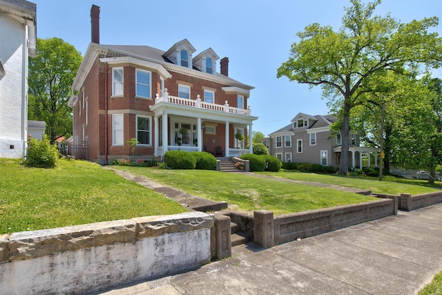 view of front of house featuring covered porch, a chimney, brick siding, and a front yard