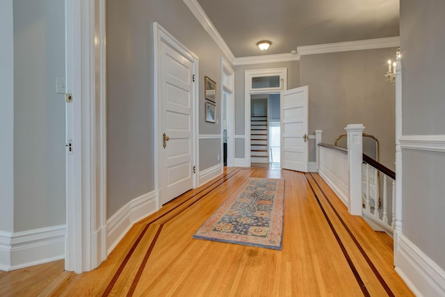 corridor featuring baseboards, ornamental molding, wood finished floors, and an upstairs landing