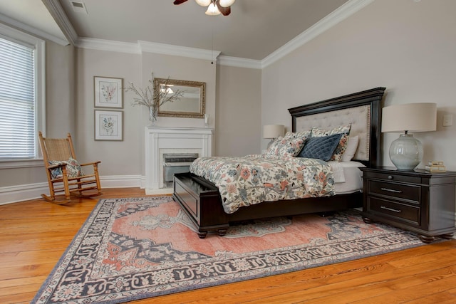 bedroom featuring baseboards, visible vents, light wood-style flooring, ornamental molding, and a fireplace