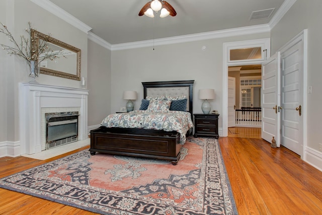 bedroom with visible vents, baseboards, light wood-style flooring, a fireplace with flush hearth, and ornamental molding