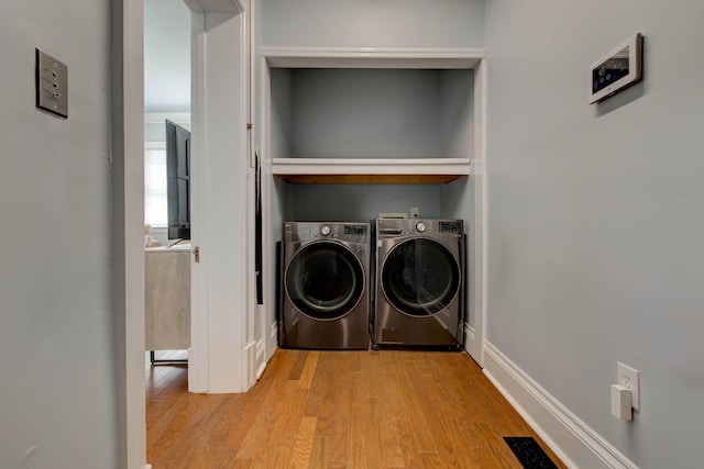 washroom featuring washer and clothes dryer, light wood-type flooring, visible vents, and baseboards