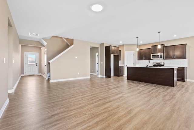 kitchen with dark brown cabinets, stainless steel appliances, a kitchen island with sink, light hardwood / wood-style floors, and hanging light fixtures