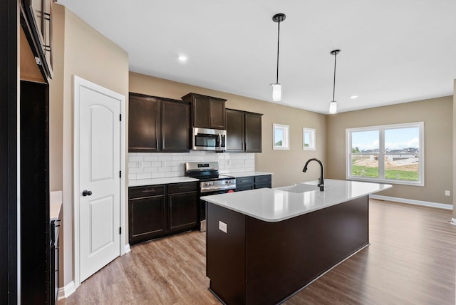 kitchen featuring appliances with stainless steel finishes, backsplash, sink, decorative light fixtures, and a center island with sink