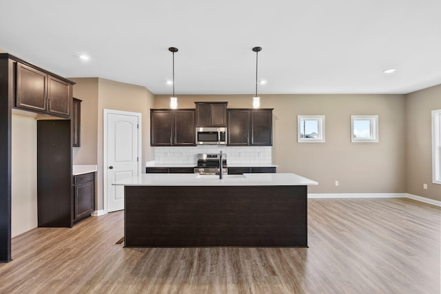 kitchen featuring sink, light hardwood / wood-style floors, pendant lighting, decorative backsplash, and appliances with stainless steel finishes