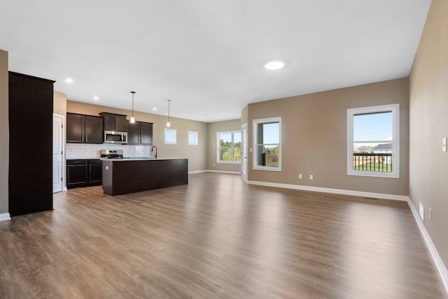 kitchen featuring hardwood / wood-style floors, a kitchen island with sink, hanging light fixtures, dark brown cabinetry, and stainless steel appliances