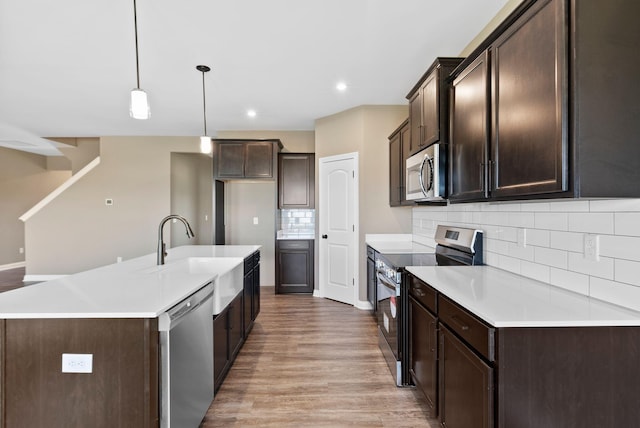 kitchen featuring pendant lighting, sink, an island with sink, appliances with stainless steel finishes, and light hardwood / wood-style floors