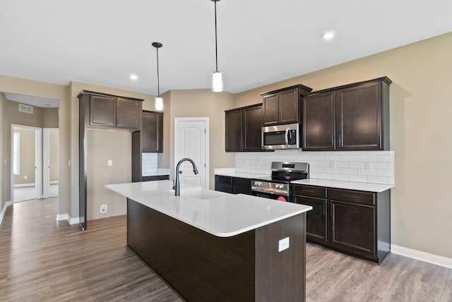 kitchen with pendant lighting, backsplash, a center island with sink, sink, and appliances with stainless steel finishes