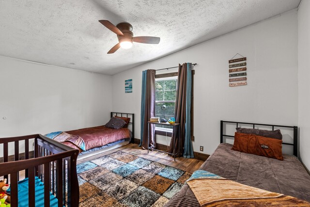 bedroom with a textured ceiling, wood-type flooring, and ceiling fan