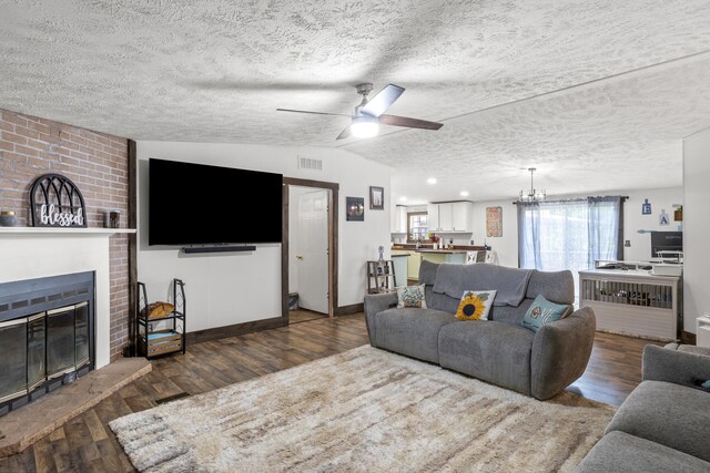 living room with vaulted ceiling, a fireplace, a textured ceiling, ceiling fan with notable chandelier, and dark hardwood / wood-style flooring