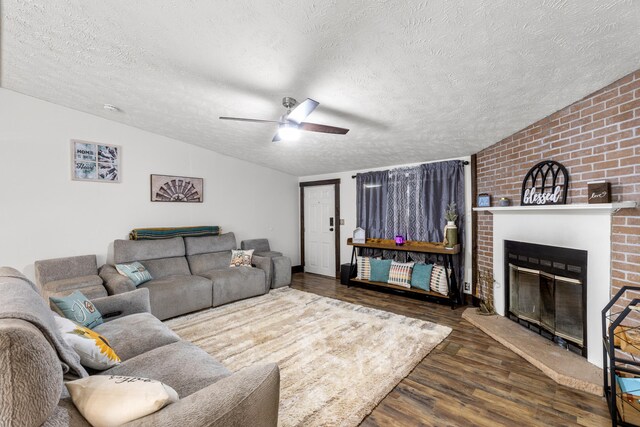 living room featuring a textured ceiling, ceiling fan, dark hardwood / wood-style floors, a brick fireplace, and brick wall