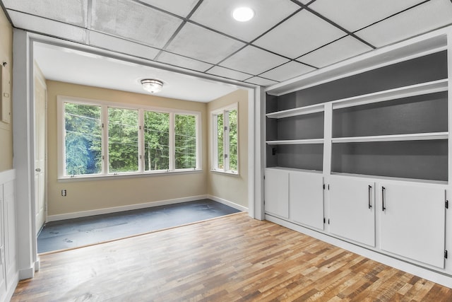 empty room featuring light wood-type flooring, built in shelves, and a paneled ceiling