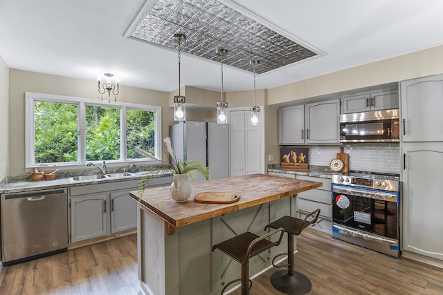 kitchen with appliances with stainless steel finishes, sink, pendant lighting, butcher block countertops, and tasteful backsplash