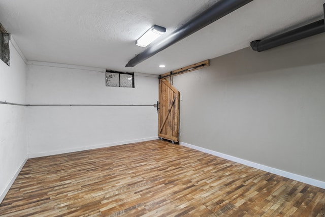 basement with a barn door, wood-type flooring, and a textured ceiling