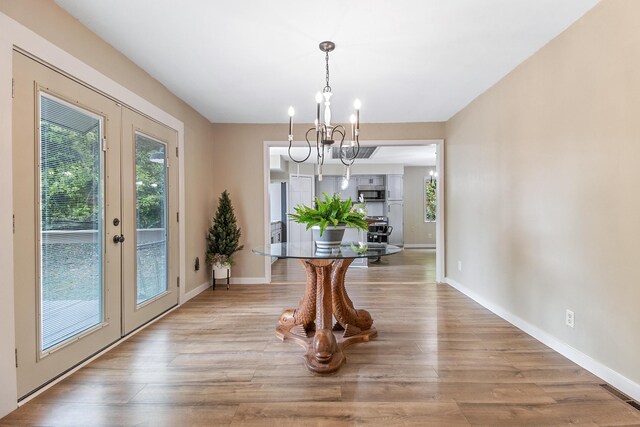 dining space with a healthy amount of sunlight, french doors, light hardwood / wood-style floors, and a notable chandelier