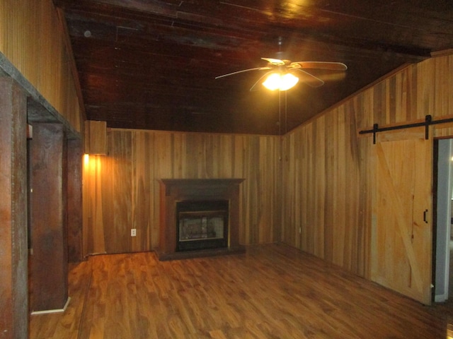 unfurnished living room featuring wood ceiling, hardwood / wood-style flooring, ceiling fan, wooden walls, and a barn door