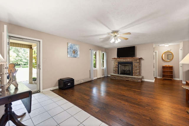 living room featuring a fireplace, a textured ceiling, light hardwood / wood-style flooring, and ceiling fan