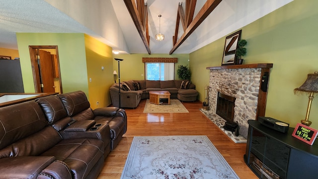 living room with vaulted ceiling with beams, a stone fireplace, a textured ceiling, and hardwood / wood-style floors