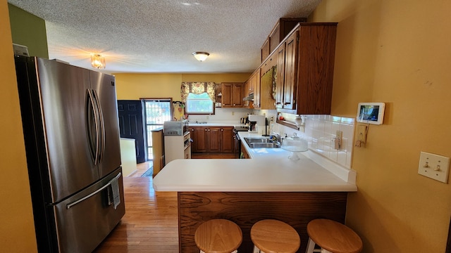 kitchen with light wood-type flooring, a textured ceiling, kitchen peninsula, backsplash, and stainless steel fridge