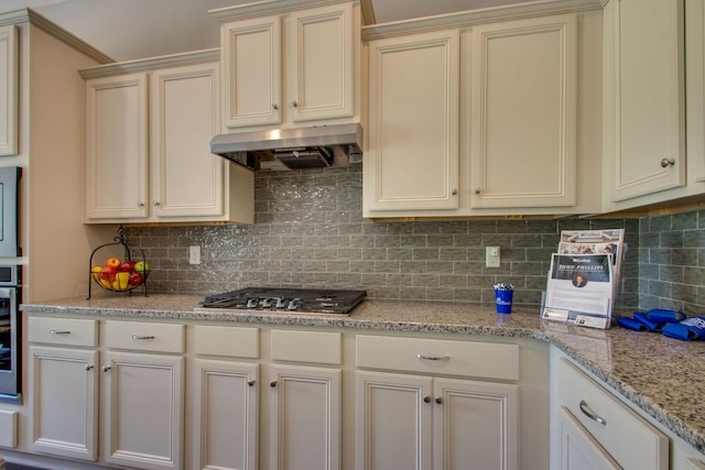 kitchen with appliances with stainless steel finishes, light stone countertops, backsplash, and cream cabinetry