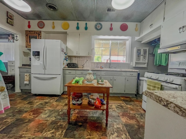 kitchen with visible vents, a sink, ventilation hood, stone finish floor, and white appliances