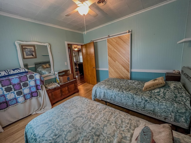 bedroom featuring crown molding, visible vents, a barn door, and wood finished floors