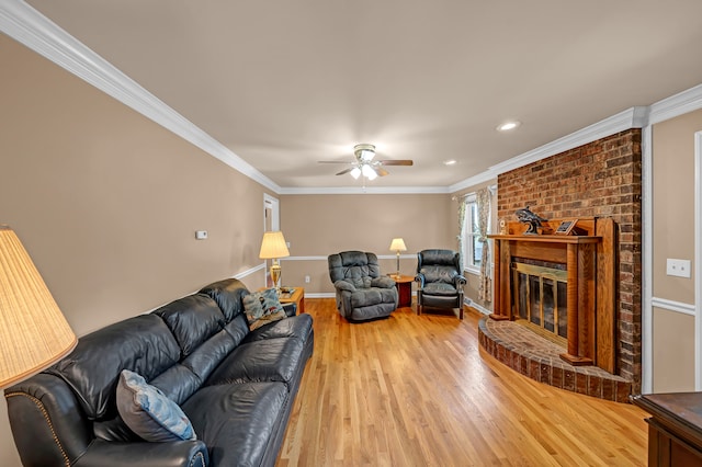 living room featuring ornamental molding, light hardwood / wood-style flooring, a brick fireplace, and ceiling fan