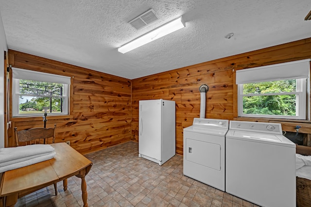 clothes washing area with washer and clothes dryer, a textured ceiling, and wooden walls