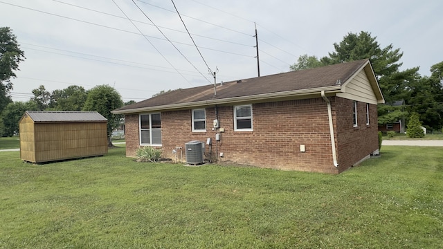 rear view of property with a yard, central AC, and a storage shed