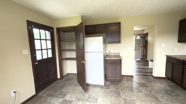 kitchen featuring white refrigerator, a textured ceiling, and dark brown cabinetry