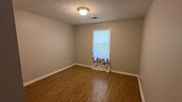 unfurnished room with visible vents, baseboards, wood finished floors, and a textured ceiling