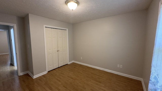 unfurnished bedroom featuring a textured ceiling, wood finished floors, baseboards, and a closet