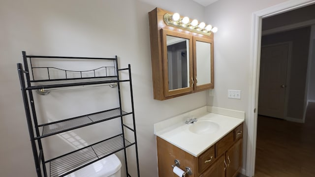 half bath with toilet, vanity, and wood finished floors