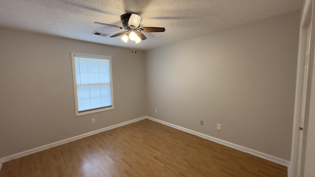 spare room with ceiling fan, a textured ceiling, visible vents, wood finished floors, and baseboards