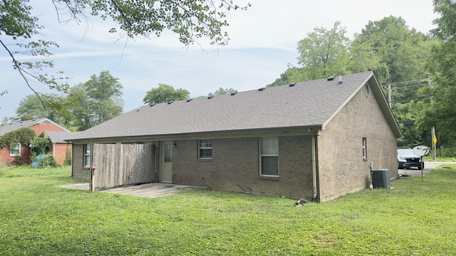rear view of house with roof with shingles, a yard, brick siding, and central AC unit